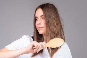 Young woman combing healthy and shiny hair, isolated on studio.