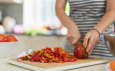 Close-up of a woman cutting Bell Pepper with a kitchen knife in a bright kitchen.