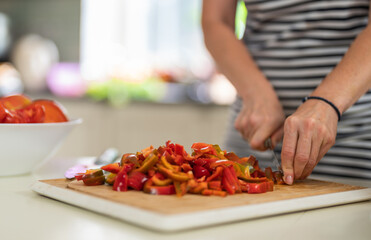 Close-up of a woman cutting Bell Pepper with a kitchen knife in a bright kitchen.