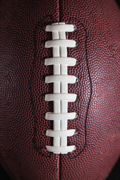 Detail shot of the cords of an american football ball. The lace is white and the ball is made of brown composite. Background is black.