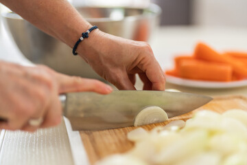 Close-up of a woman cutting onions with a kitchen knife in a bright kitchen.