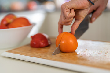 Close-up of a woman cutting an orange tomato with a kitchen knife in a bright kitchen.