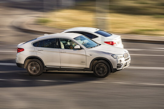 Fast moving white BMW X4 on city road. Compliance with speed limits on the streets. Side view shot of driving SUV