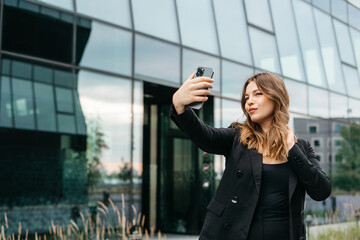 Portrait of charming positive blonde young woman taking selfie on city background, travel concept for students