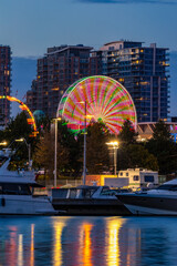 Ferris wheel in motion at night, reflecting in water around boats. Canadian National Exhibition 
