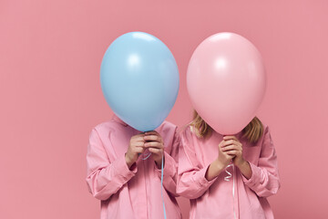 school-age children stand holding balloons in their hands, covering their faces with them....