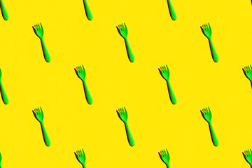 a pattern of green plastic forks on an yellow background with a hard light, top view