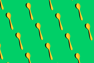 a pattern of yellow plastic spoons on an green background with a hard light, top view