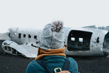 Woman on winter clothes in front of the wreck of th crashed airplane in Iceland, on the beach of...