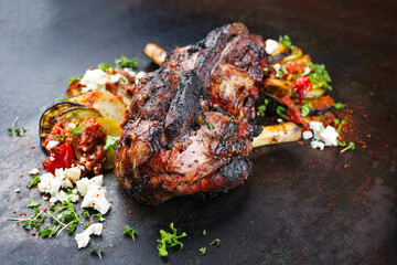 Traditional Greek barbecue lamb shank with vegetable briam served as close-up on a rustic black board
