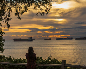 Silhouette of young woman standing by the beach at sunset. Seascape with ships at sunset with beautiful cloudy sky