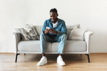 Black Male Using Phone Texting Sitting On Couch At Home