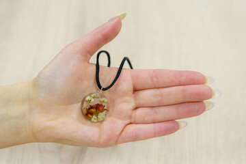 Transparent pendant with flowers in the palm of a female hand. Homemade epoxy resin jewelry