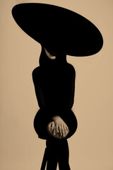 Fashion style. Abstract woman black body silhouette with big hat and black clothes sitting on...