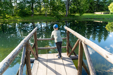 preschooler boy is resting, leaning on the wooden bridges of the pond