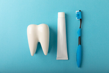 Toothbrush and toothpaste with tooth model on blue background with copy space. Flat lay. Oral hygiene. Oral Care Kit. Dentist concept.