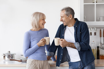 Obraz premium Loving senior couple in homewear drinking coffee at kitchen