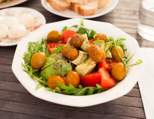 fresh salad of arugula, avocado, cherry tomatoes with olives in white bowl