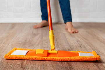 Barefoot woman mopping the floor. Female cleaning the wooden laminate floor with orange microfiber...