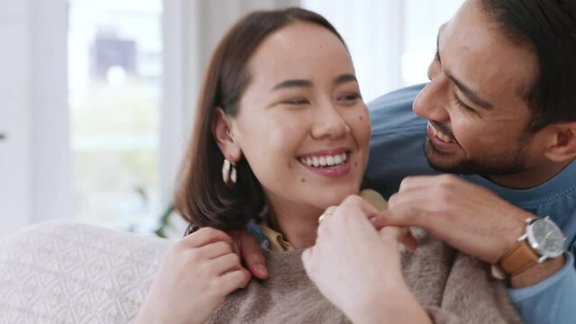 Love, happiness and fun with asian couple being playful and affectionate while laughing and tickling on the sofa at home. Happy man and woman bonding and joking together in a healthy relationship