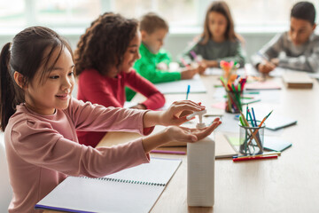 Asian Schoolgirl Disinfecting Hands Learning With Classmates In Classroom