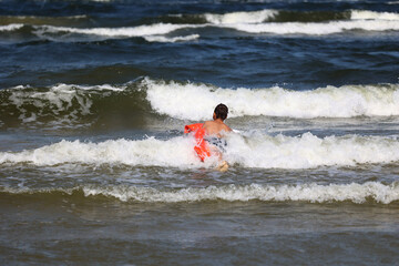 Dziecko z materacem dmuchanym wchodzi do morza na fale