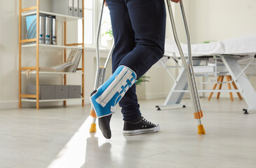 Close up of injured man with broken leg in bandage walk with crutches at home. Unwell guy with splint on foot after accident or trauma make first steps. Rehabilitation. Medicine and healthcare. - obrazy, fototapety, plakaty