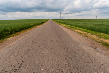 Fototapeta na wymiar An empty roadway outside the city passes by a rural field and a blooming meadow. Travel by car away from the city and the hustle and bustle. Paved road on a sunny day without cars.