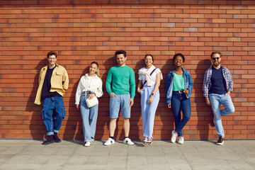 Stylish and cool different young people stand in row and pose against background of brick wall on...