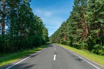 Fototapeta na wymiar A new modern asphalt road passing through the forest. An empty country road in the woods. High-quality conditions for cargo and passenger transportation.