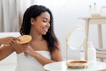Beautiful African American Woman Combing Her Curly Hair With Bamboo Brush At Home
