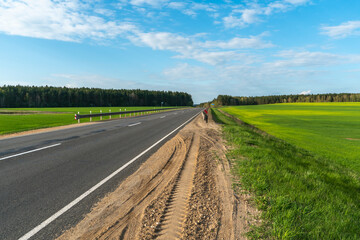 An empty roadway outside the city passes by a rural field and a blooming meadow. Travel by car away...