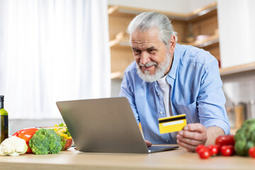 Fototapeta premium Senior Man Using Laptop And Credit Card In Kitchen, Ordering Groceries Online