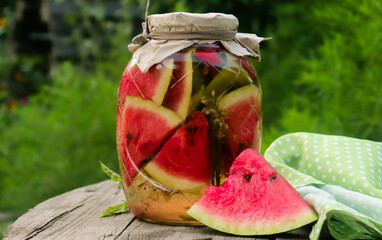 pickled pieces of red watermelon in a glass jar on a wooden table in the garden in summer selective...