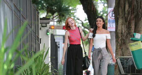 Two female multiracial friends walking in sidewalk city