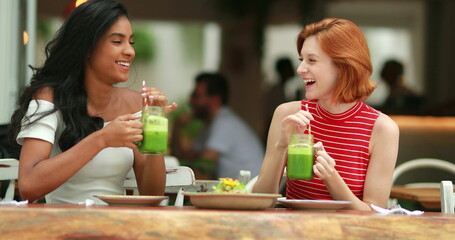 Two female friends drinking green detox juice and eating healthy salad. multiracial friendship