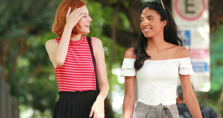 Obraz premium Two multiracial female friends walking in city, candid smiling and laughing
