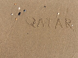 on the beach is carved with letters in the smooth sand the writing Qatar