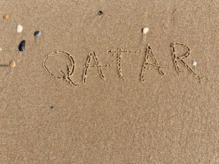 on the beach is carved with letters in the smooth sand the writing Qatar