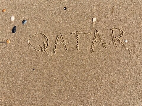 on the beach is carved with letters in the smooth sand the writing Qatar