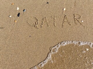 on the beach is carved with letters in the smooth sand the writing Qatar