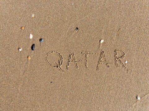 on the beach is carved with letters in the smooth sand the writing Qatar