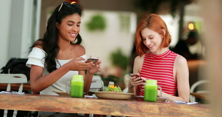 Two beautiful multiracial girls seate holding cellphone showing screen to friend