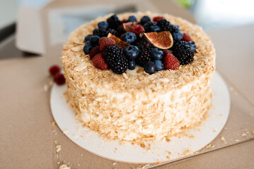 Savoyardi berry cake garnished with blackberries,blueberries and fresh figs on a wooden stand with hydrangea flowers on wooden table.Close up of cake in rustic style.
