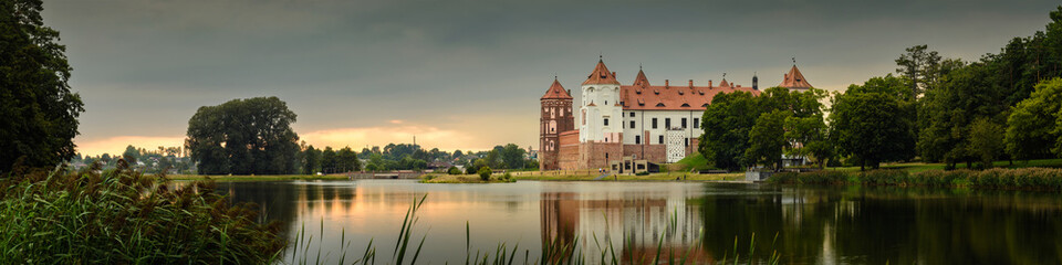 Mir Castle, Belarus. Scenic panoramic view of the complex across the lake with reflections on the water in the evening twilight. UNESCO world heritage
