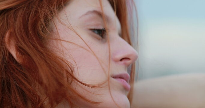 Profile of redhead young woman stretching neck feeling wind outside