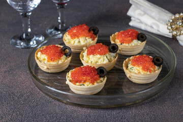 Tartlets with red caviar, egg and melted cheese, decorated with black olives