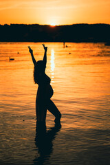 black silhouette of a pregnant woman with a baby bump or belly raising her arms in the air to make...