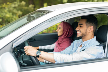Fototapeta na wymiar Happy millennial muslim wife in hijab and husband driving car at steering wheel, enjoy journey