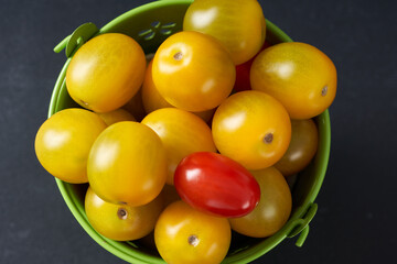 Yellow cherry tomatoes in a green mini bucket on a dark background.